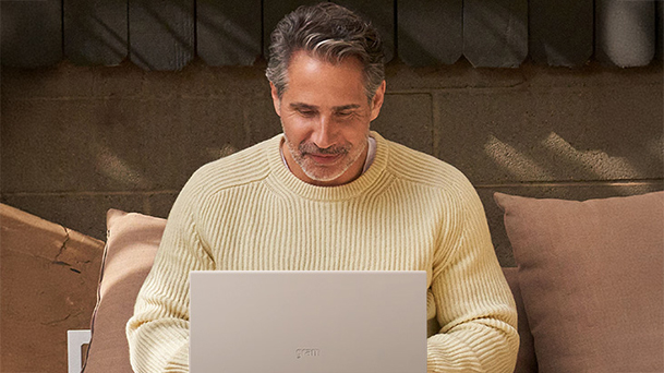 L'image montre un homme vêtu d'un pull jaune assis sur un canapé, travaillant sur un ordinateur portable avec une copie de la mention « Les grandes entreprises ont déjà déployé les nouveaux ordinateurs Windows 11 Pro ».
