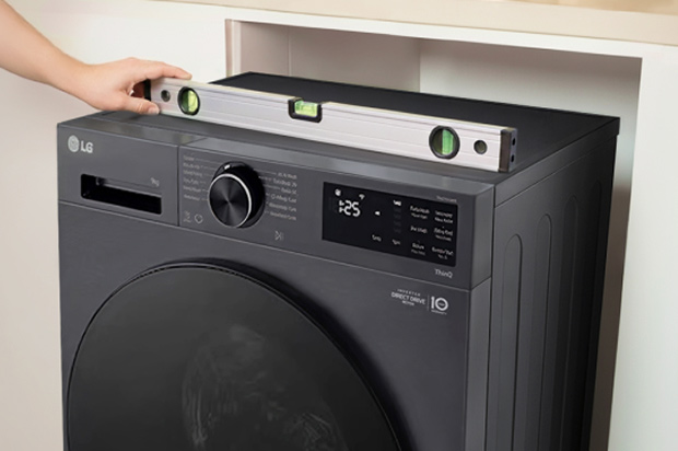 Black LG washing machine with a spirit level placed on top to check that the appliance is horizontally aligned.	