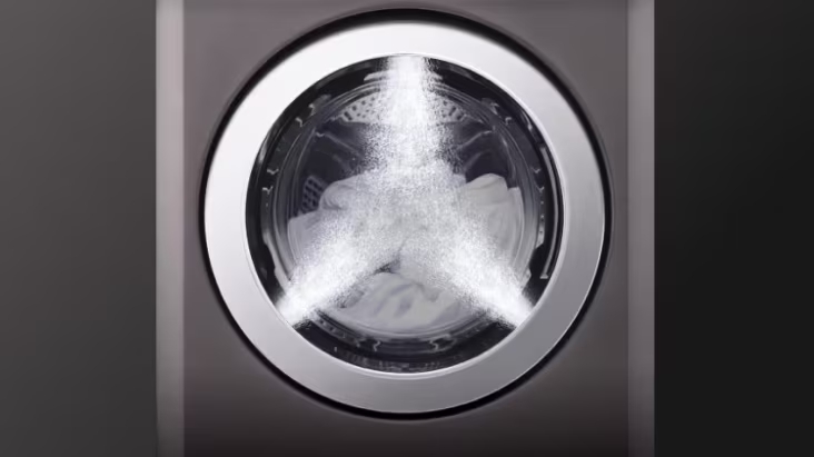 Front view of a commercial washer during operation with water spray evenly cleaning laundry	