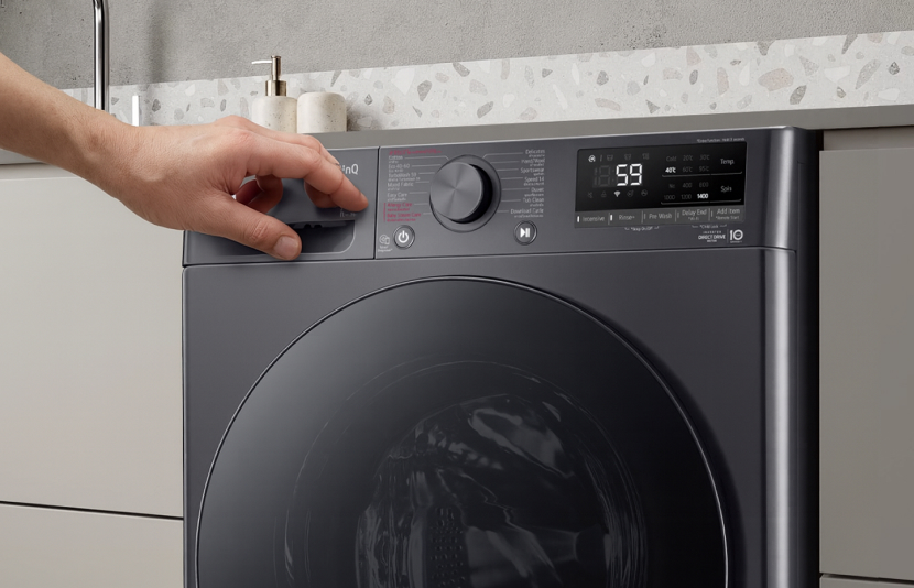 LG front load washing machine with hand adjusting temperature dial in a modern kitchen-style laundry space	