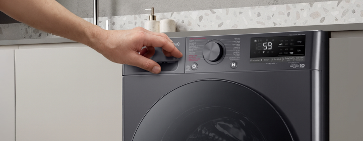 LG front load washing machine with hand adjusting temperature dial in a modern kitchen-style laundry space	