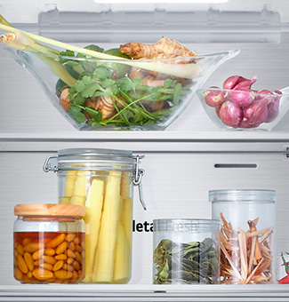 Close-up view of the bottom freezer shelf of an LG with fresh herbs, vegetables and preserves in glass containers.