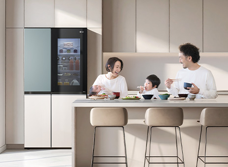 LG's InstaView refrigerator freezer in a bright kitchen. Inside the door is orange juice. A man and a woman are looking at their mother, with a child wearing a white shirt in between.