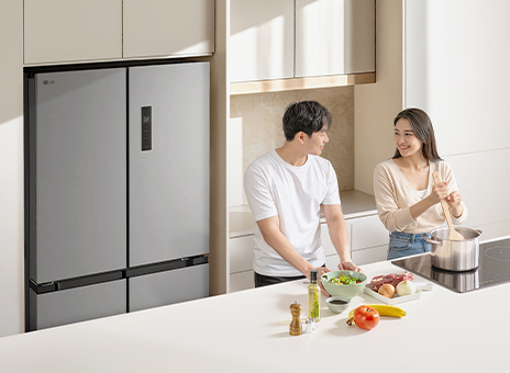 A large dark graphite LG refrigerator freezer with spacious storage in a stylish kitchen. A man and a woman cook in front of a table.