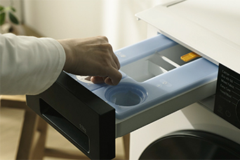 Close-up of a hand near the blue detergent compartment of a white LG washing machine.