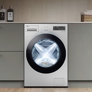 A white LG washing machine is neatly installed under a laundry counter. Inside the drum, water sprays from four directions during the washing process.