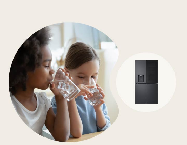 Two children drinking water at a table with an LG refrigerator and built-in dispenser in the background