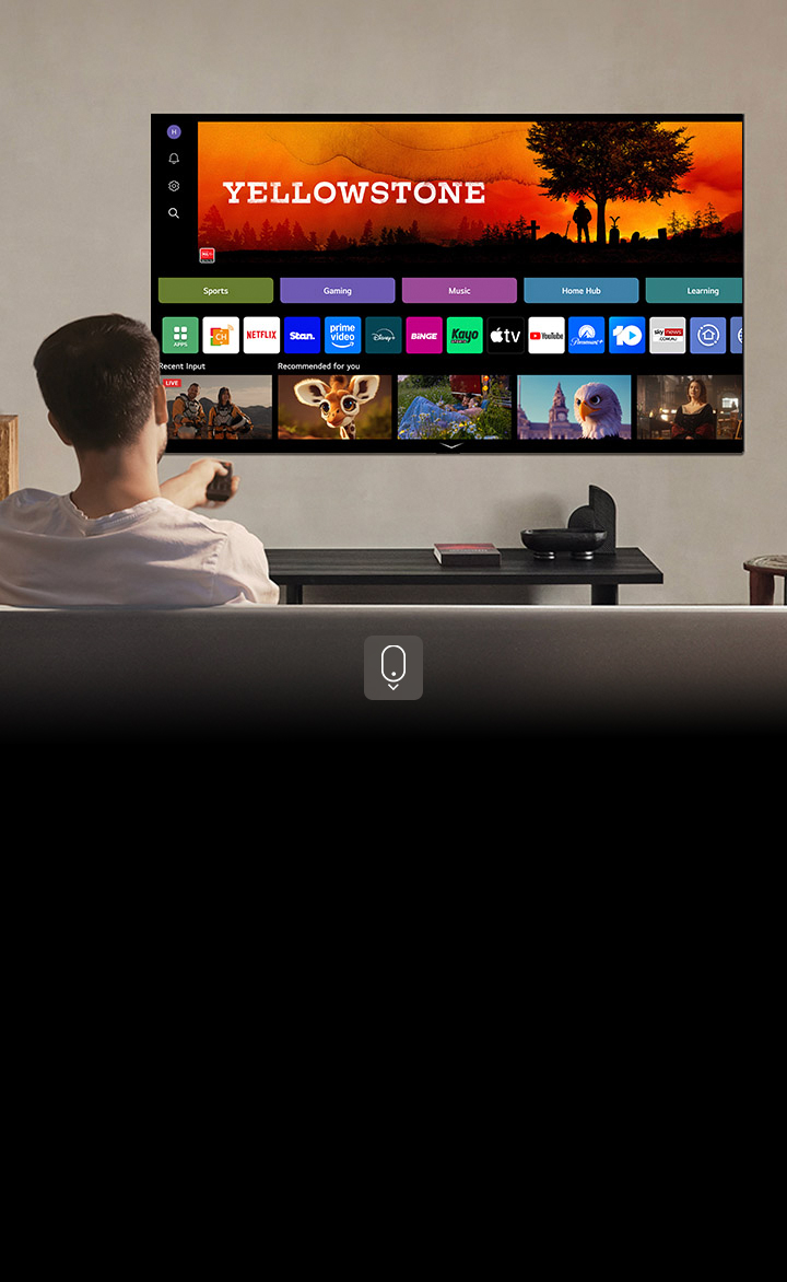 Person on the couch holding out a remote control. LG AI TV on the wall with LG webOS on the screen.