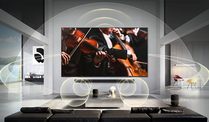 LG Micro RGB evo AI MRGB95 with WOW Orchestra displays a concert scene with a soundbar below the screen, while graphic sound waves extend across the living room to convey synchronized, surround sound. 
