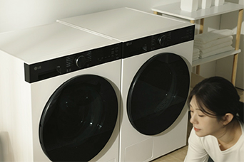 Woman enters carrying a laundry basket and loads clothes into the large capacity LG washing machine.