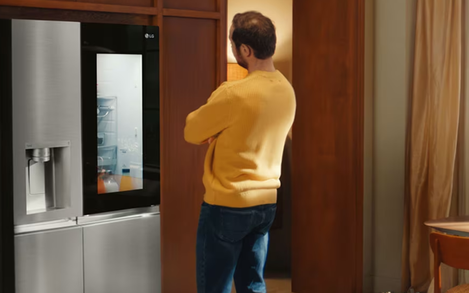 A man in a yellow jumper admires an LG fridge with an illuminated InstaView™ panel, allowing him to see inside.