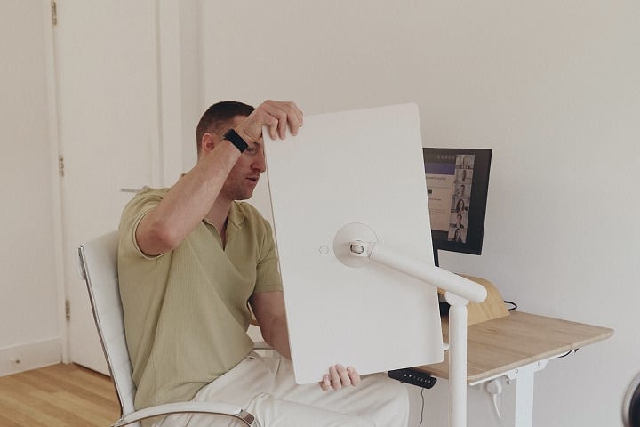 A man sitting on a chair and rotating a StanbyME smart screen to a 90-degree angle.