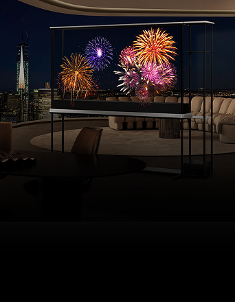 A transparent LG TV displays vivid fireworks in a high-rise luxury living room at night, with the city skyline visible in the background.