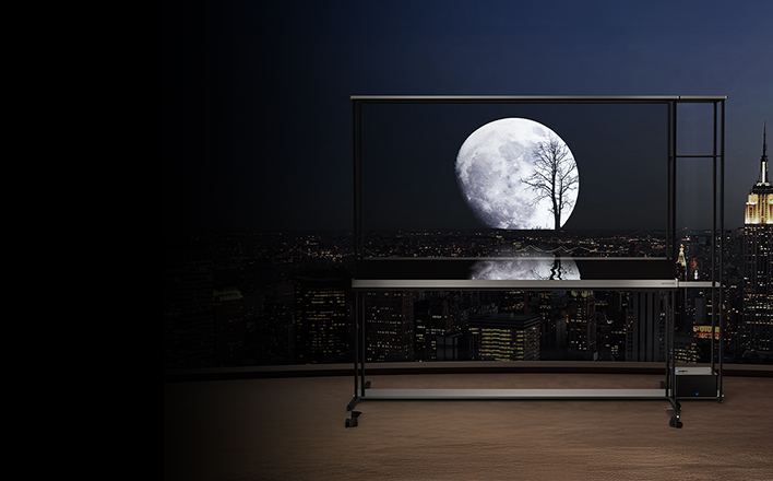 Transparent TV on balcony at night displaying full moon and tree silhouette over city skyline.