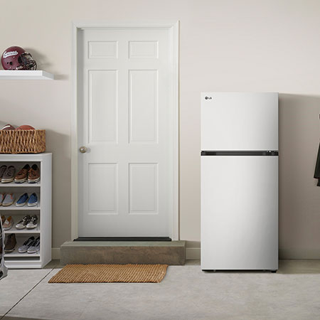 The white finish LG 28-inch 18 cu.ft. Top Freezer Refrigerator LT18S2100W, shown placed in a garage setting.