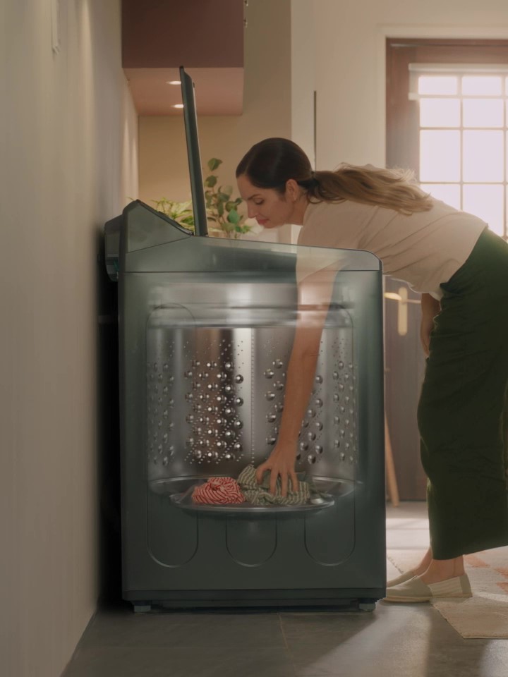 Black steel LG top-load washing machine with a glass lid and a person reaching inside the drum.
