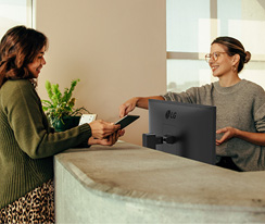 Friendly receptionist showing a woman where to sign on a digital tablet.