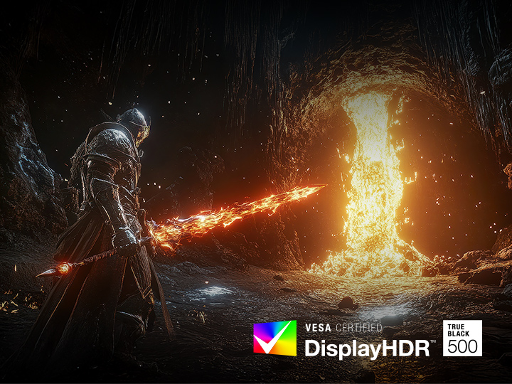 A heavily armored warrior stands in a dark, rocky cavern wielding a glowing, fiery sword. In front of the warrior, a massive torrent of molten lava pours down from the cave ceiling, casting a bright, intense orange light across the scene. The contrast between the darkness of the cave and the blazing fire emphasizes the game's dramatic and cinematic visual style.