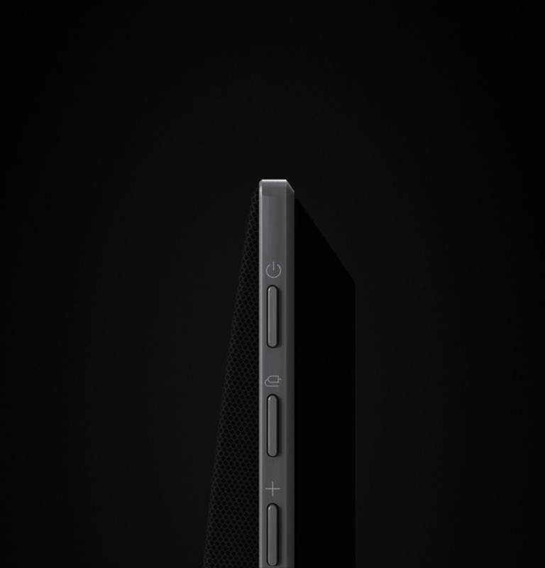 LG Soundbar is against a black backdrop opens to show the soundbar's side buttons, pans out, rotates to reveal its full design. The black backdrop transitions into a wall with an LG TV, and the soundbar mounts against the wall. 	