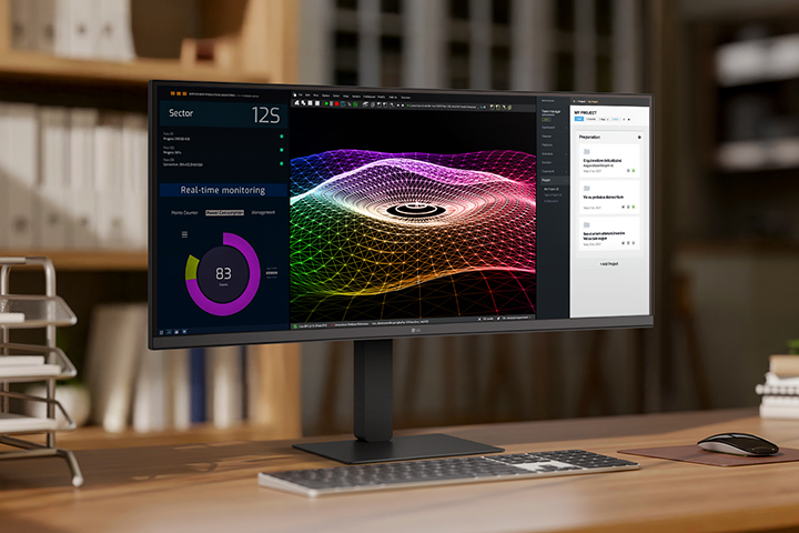A modern home office setup featuring a large ultra-wide LG monitor displaying data dashboards, 3D graphics, and project management tools, with a wireless keyboard and mouse on a wooden desk.