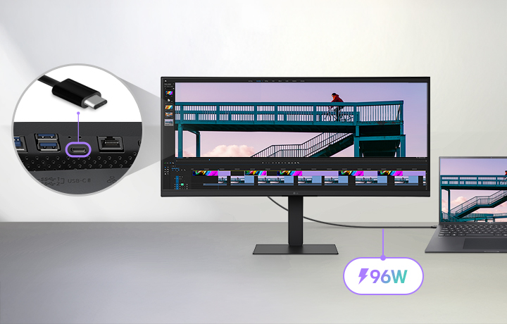 UltraWide monitor connected to a laptop via a USB-C cable, displaying a video editing project with a cyclist on a bridge, featuring a close-up of the USB-C port and highlighting 96W power delivery capability.