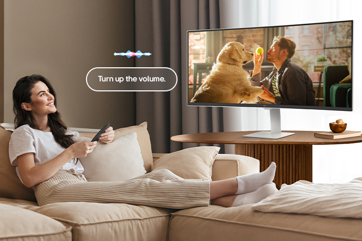A woman is turning up the LG Smart Monitor’s volume using a Magic Remote.