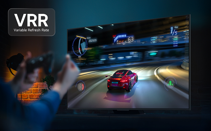 Des mains tenant une manette de jeu devant un téléviseur avec un jeu de course automobile à l’écran. Le logo VRR (taux de rafraîchissement variable) est visible.