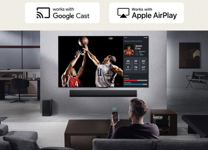 Personne dans son salon tenant son téléphone. Sur le téléphone se trouve une icône de transmission indiquant que l’écran du téléphone est reflété sur le téléviseur. Un match de basket-ball est diffusé sur le téléviseur. Sur le côté, un écran miroir affiche les statistiques des joueurs.