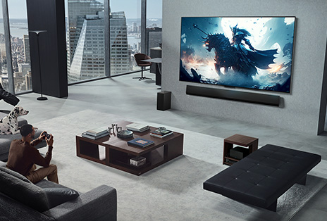 Salon avec une personne jouant à un jeu vidéo sur son téléviseur mural sans fil de LG et sa LG Soundbar. Il tient une manette dans sa main, mais la console de jeu n’est pas immédiatement visible. Il n’y a pas non plus de câbles visibles. La Zero Connect Box est cachée, à peine visible, sous une table d’appoint.