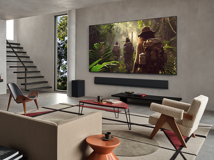 Vue large d’un salon à l’intérieur d’une maison haut de gamme, un couple regarde un film sur leur LG OLED TV fixé au mur. La conception du téléviseur s’intègre élégamment au mur et à la décoration intérieure.