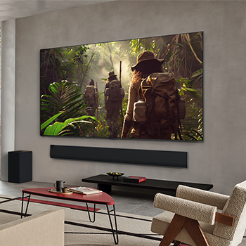 Vue large d’un salon à l’intérieur d’une maison haut de gamme, un homme regarde un film sur son LG OLED TV fixé au mur. La conception du téléviseur s’intègre élégamment au mur et à la décoration intérieure.