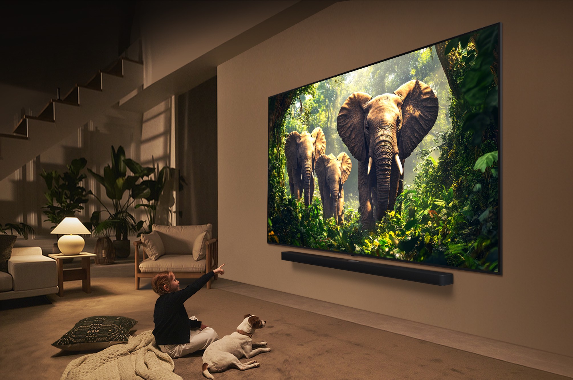 Une fille et un chien sont assis devant un LG QNED TV accroché au mur et représentant trois éléphants marchant vers l’extérieur, au-dessus d’une LG Soundbar. Le titre met en avant comment chaque action devient plus captivante sur un écran géant.
