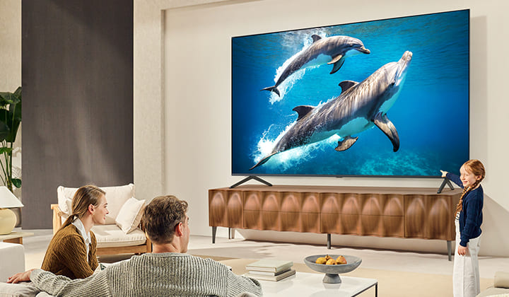 Une fille et un chien sont assis devant un LG QNED TV accroché au mur et représentant trois éléphants marchant vers l’extérieur, au-dessus d’une LG Soundbar. 