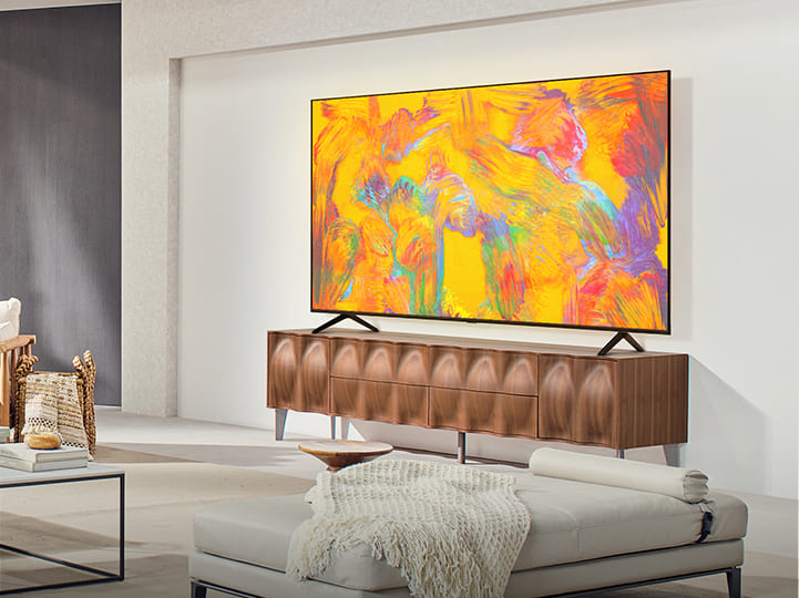 Le LG QNED TV est au-dessus d’un tiroir TV dans un espace de vie confortable. Le LG QNED TV représente un arrière-plan abstrait dans les tons orange, jaune, violet et rose.
