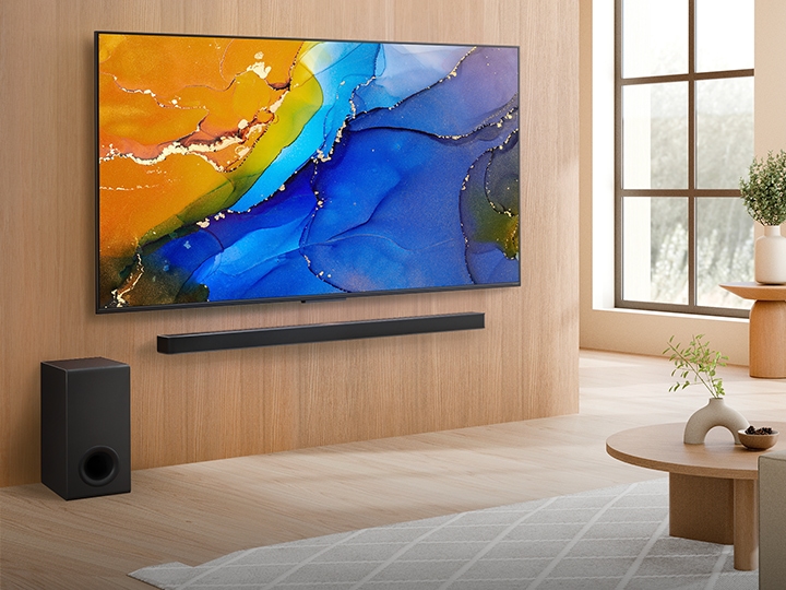 LG QNED TV monté sur un mur au-dessus d’une LG Soundbar dans un salon moderne. LG QNED TV représente un arrière-plan abstrait et coloré.	