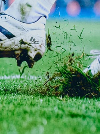 Gros plan d’herbe et de terre projetées lors d’une action de football