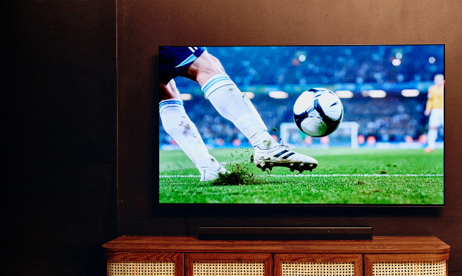 Grand téléviseur diffusant un match de soccer au-dessus d’un meuble TV en bois dans un salon chaleureux.