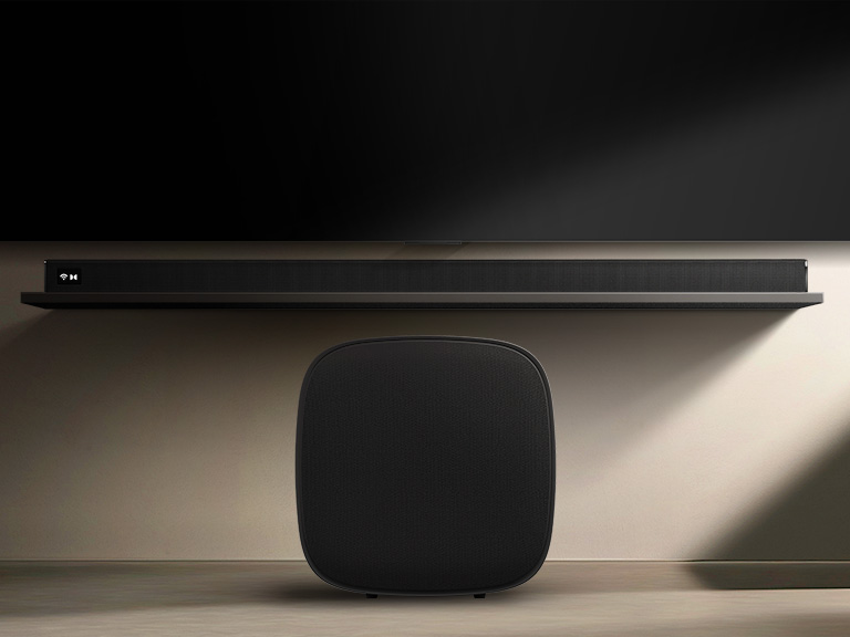 Le caisson de basses W7 du système Sound Suite de LG est placé sous un téléviseur avec une barre de son pour montrer à quel point il est facile d’élargir le son sans fil pour obtenir un système audio stéréo maison immersif.