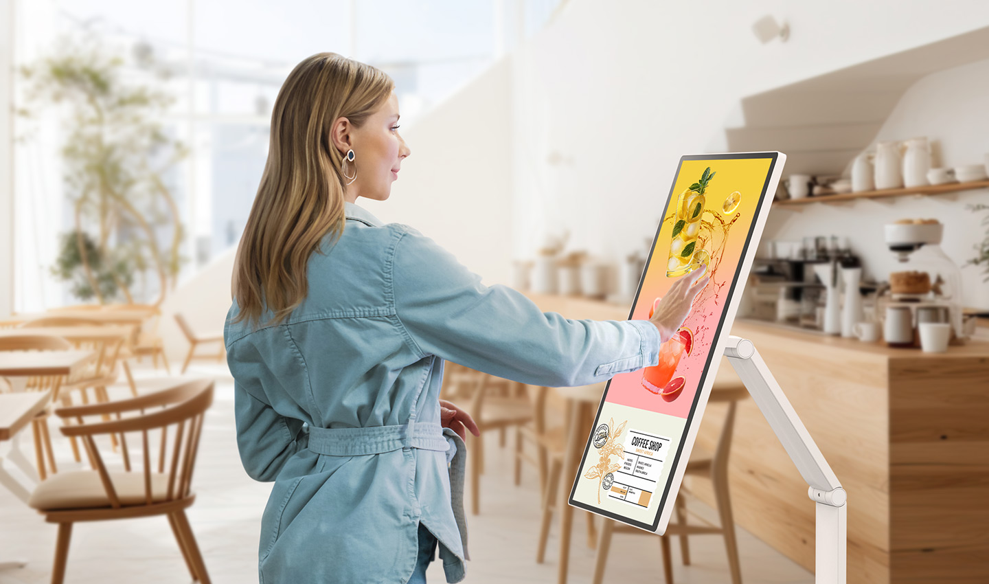 Une femme regarde une bannière d'événement affichée sur un LG Smart Monitor Swing dans un café.
