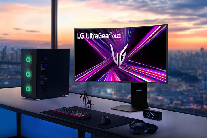 Moniteur LG UltraGear OLED sur un bureau de jeu avec configuration PC, vue sur un paysage urbain au coucher du soleil.