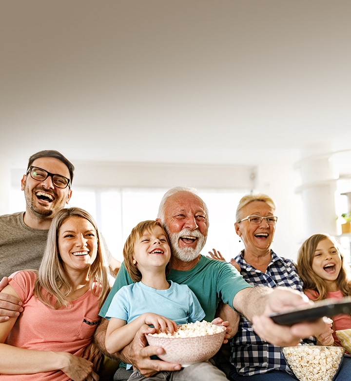 Une famille rigole pendant que le grand-père pointe la télécommande vers l’extérieur.