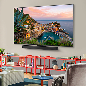 منظر واسع لغرفة معيشة أنيقة وملونة. تلفزيون LG OLED evo AI C5 4K Smart TV مثبت على الحائط مع مكبر صوت LG Soundbar أسفله. يتناغم تصميم التلفزيون بشكل جيد مع المساحة. يوجد على شاشة التلفزيون عمل فني ملون. 