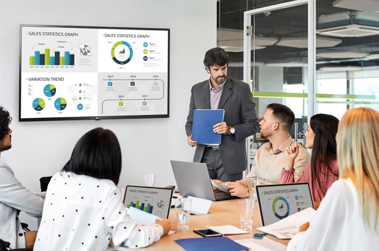 There are 6 people having a meeting and 4 PC screens are simultaneously shared on large signage hanging on the wall through the USB dongle device connected to the personal PCs.