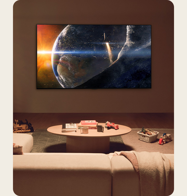 A family sat on the floor of a low-lit living room by a small table, looking up at an LG TV mounted on the wall showing the Earth from space.