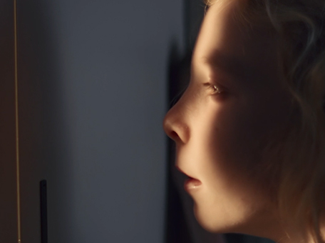 A close-up shot of a girls face, partially in shadow, partially illuminated as she peers out from a hiding place.