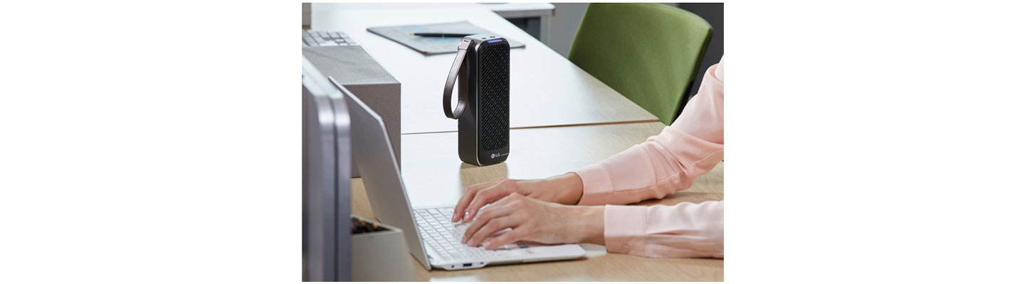 A person working on their laptop uses PuriCare™ Mini Air Purifier on the desk to keep the working environment pleasant.