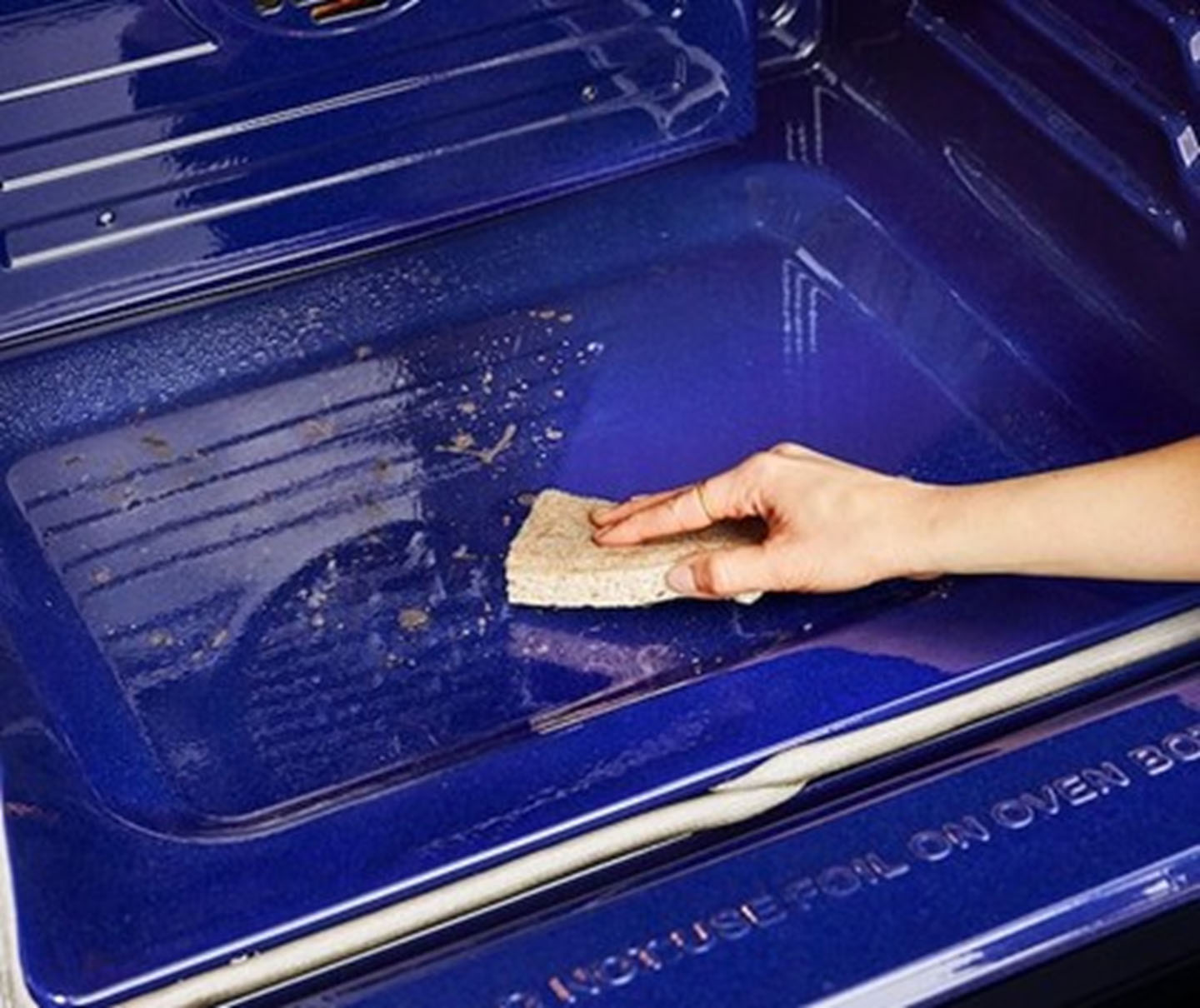 A hand reaches out to wipe the interior surface of an LG EasyClean™ oven with a sponge.