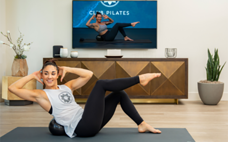 A woman exercising on her living room floor as she watches a Club Pilates class on her LG TV