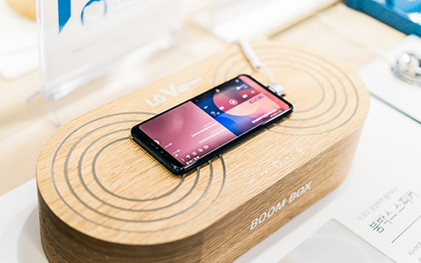 An LG V40 ThinQ is on display at a promotional zone, demonstrating its powerful amplification when placed on a solid surface or box.