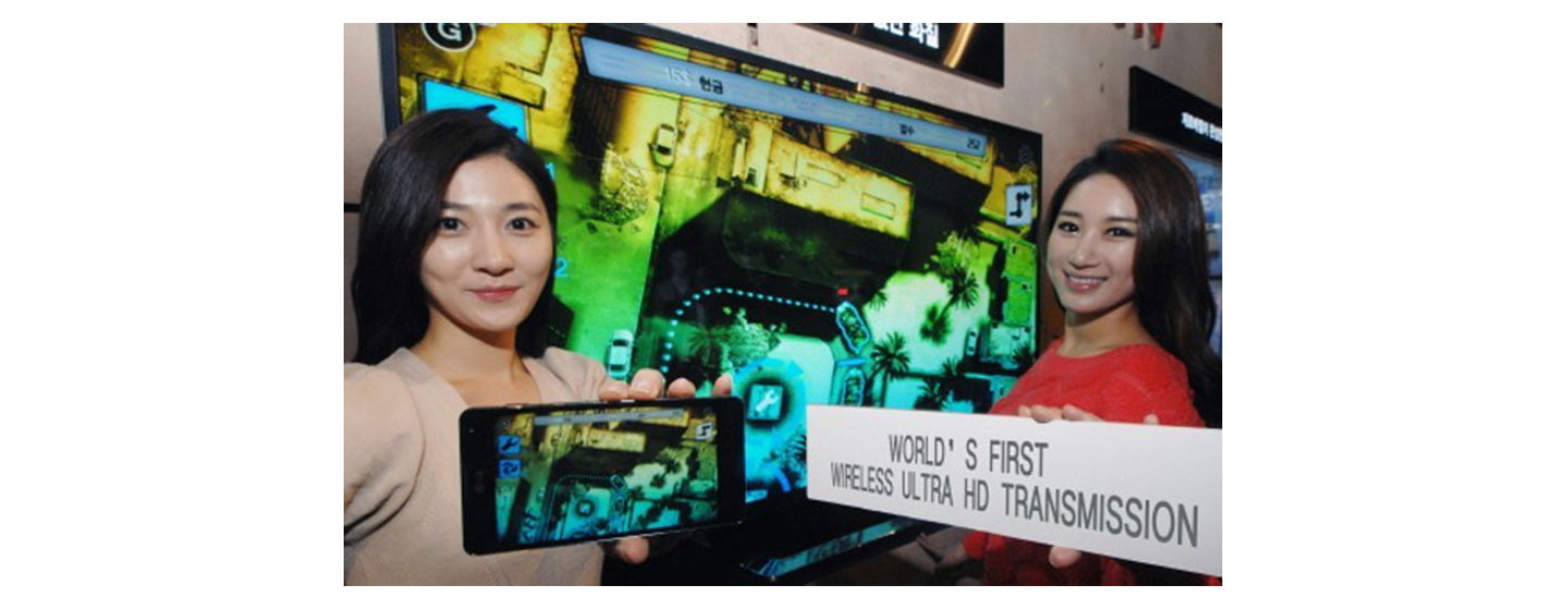 Two women hold up an LG phone and banner highlighting the world’s first wireless Ultra HD Transmission technology